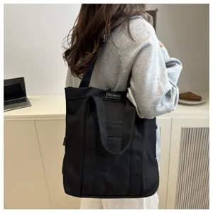Modern black canvas tote bag worn on shoulder in a stylish indoor setting