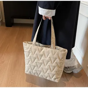 Vista detallada de un bolso tote acolchado beige con costuras en V y tela suave