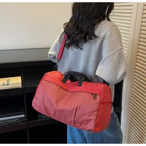 Detail view of a stylish red large capacity travel bag with grid pattern carried by a model