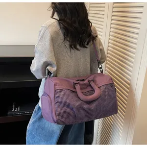 Model carrying a large purple checkered duffel bag on shoulder in an indoor setting