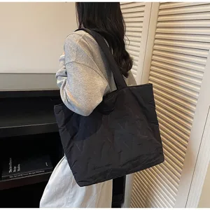 Vista detallada de un bolso tote acolchado negro grande usado por una modelo en sala