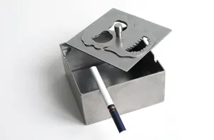 Vista dettagliata di posacenere metallico con coperchio rotante e motivo di teschio