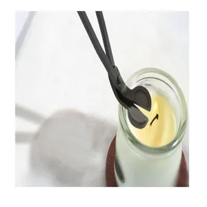 Close-up of black stainless steel wick trimmer being used on a lit jar candle.