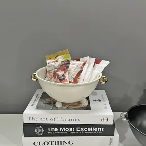 Detailaufnahme einer cremefarbenen Eisen-Obstschale mit Goldgriffen auf Dekobüchern