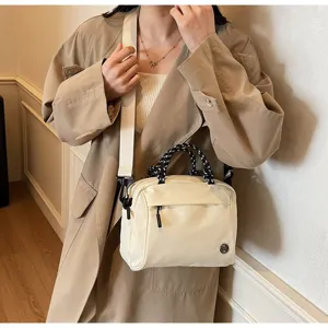 Stylish cream crossbody bag with black rope handles and adjustable strap worn by model