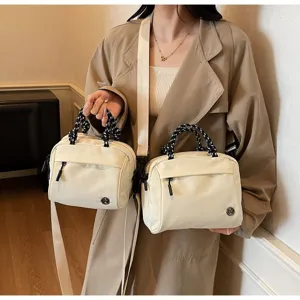 Detail showing two sizes of beige crossbody bags with braided handles and metal logo.