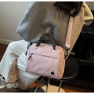 Detail of minimalist pink handbag with patterned rope handles and crossbody strap.