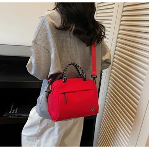 Model wearing a red nylon crossbody bag with braided handle and shoulder strap