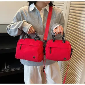 Vibrant red lightweight nylon crossbody bag held by a model in casual grey sweater outfit