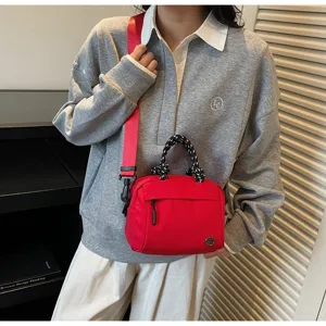 Detailed shot of a red nylon crossbody bag with unique black and white braided handle