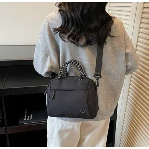 Detail view of a minimalist black nylon crossbody bag with woven handle on model