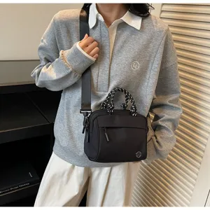 Black lightweight crossbody bag with woven handles shown in a lifestyle model shot