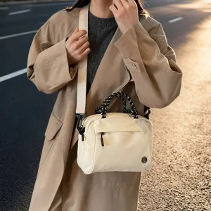 Lifestyle view of a cream multi-compartment handbag worn with a classic trench coat
