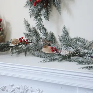 Künstliche Weihnachtsgirlande mit verschneiten Zweigen und roten Beeren auf Kamin