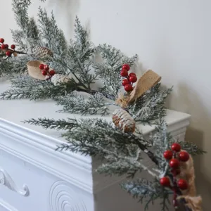 Nahaufnahme einer beflockten Weihnachtsgirlande mit roten Beeren und Tannenzapfen