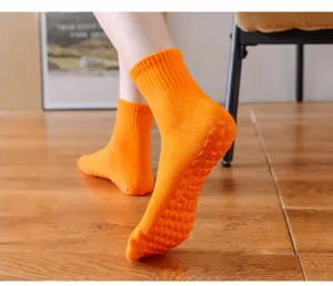 Detailansicht orangefarbener Baumwollsocken mit rutschfesten Gummigriffen an der Sohle.