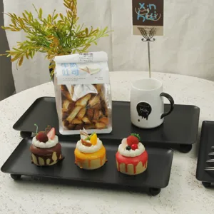 Elegant black rectangular serving tray with ball feet displaying mini cakes on a table