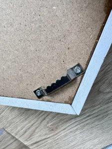 Close-up detail of a sturdy metal sawtooth hanger on white wooden frame backboard