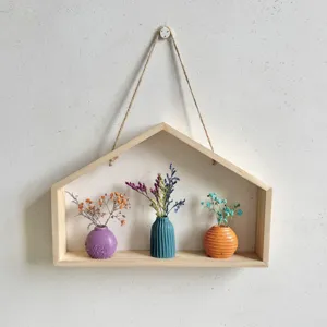 Detail van houten wandplank in huisvorm met kleurrijke keramische vazen en droogbloemen.