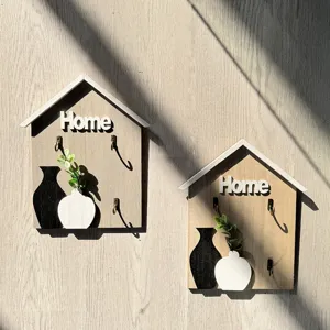 Detail of house-shaped wooden key holders with Home text and vase decorative plant.