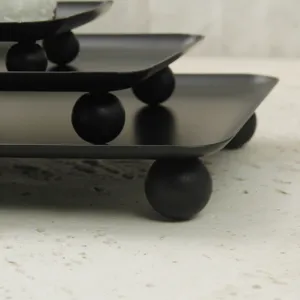 Close-up of minimalist matte black rectangular tray featuring modern spherical ball feet