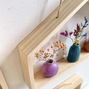 Detail van een houten wandplank met een kleine paarse vaas en prachtige droogbloemen