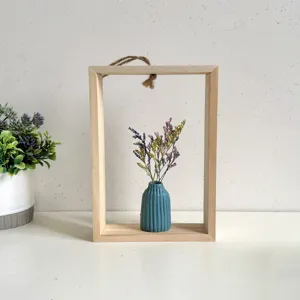 Detail van houten wandframe in INS-stijl met blauwe keramische droogbloemenvase.