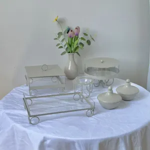 Elegante juego de soportes para postres crema sobre mantel blanco con flores decorativas.