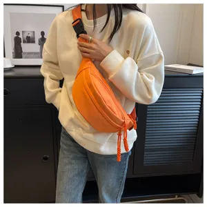Detailed shot of vibrant orange crossbody chest bag with wide strap and braided zip pulls
