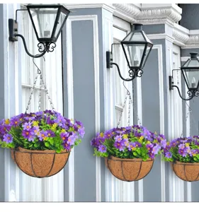 Tre cesti di fiori artificiali appesi con margherite viola esposti su una parete vintage.