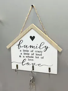 Nahaufnahme eines schlüsselschranks aus holz in hausform mit familienspruch und haken