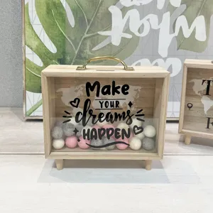 Close-up detail of wooden money box with 'Make YOUR dreams HAPPEN' quote and felt balls