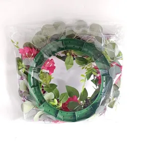 Artificial pink and purple rose wreath with green leaves in clear plastic packaging