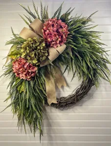Detailed view of a farmhouse hydrangea wreath with green leaves and a rustic burlap bow.