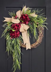 Rustic artificial hydrangea wreath with green foliage and burlap bow on a black door