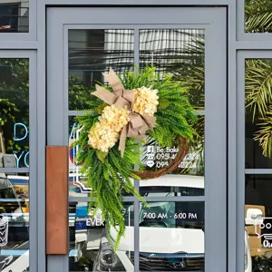 Elegant artificial hydrangea wreath with a burlap bow hanging on a stylish glass door