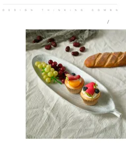 Detail view of leaf-shaped white snack platter with fresh fruit and cupcakes on linen