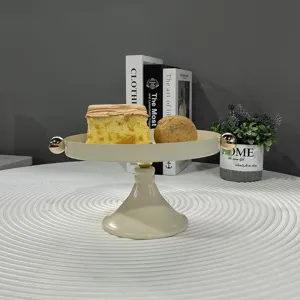 Beiger Tortenständer aus Eisen mit goldenen Kugeln und Gebäck auf einem weißen Tisch