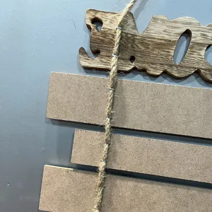 Dettaglio di un cartello da parete in legno rustico con corda di canapa sul retro.