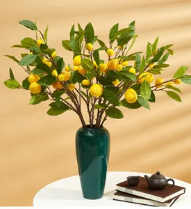 Artificial lemon branches in a dark green vase on a table for elegant home decor.
