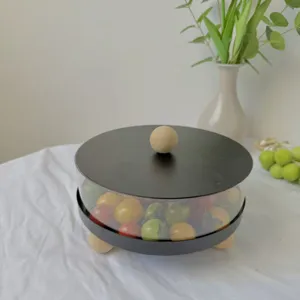 Detalle de frutero redondo minimalista con tapa negra y pomo de madera con tomates