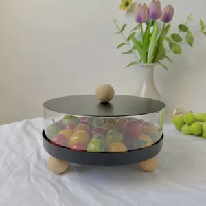 Frutero redondo de acrílico con tapa negra y patas de madera sobre mesa