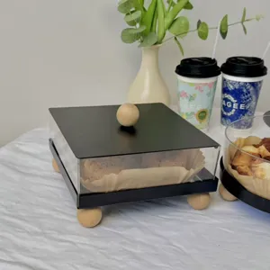 Square acrylic dessert display box with black lid and minimalist wooden ball handle.