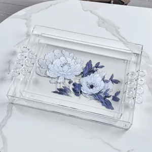 Dettaglio vassoio in acrilico trasparente con manici di perle e motivo floreale blu.
