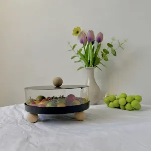 Detalle de un frutero redondo de acrílico con tapa y patas esféricas de madera natural