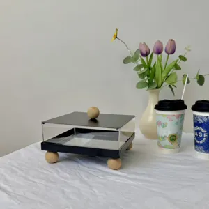 Professional macro detail view of minimalist square acrylic dessert display box with wooden legs.