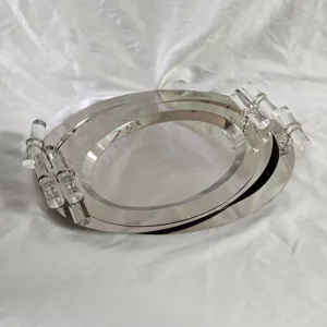 Detail of oval stainless steel mirror tray with crystal-like handles on white fabric.