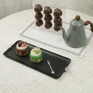 Detail einer cremefarbenen, schwarzen Torte-Platte aus Eisen mit weißen Steingriffen.