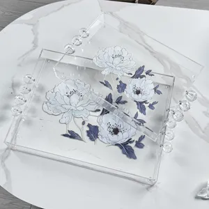 Set di due eleganti vassoi in acrilico trasparente con manici a sfera e motivo floreale.