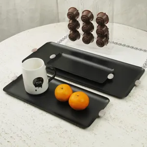 Drei elegante mattschwarze rechteckige Metalltabletts, präsentiert mit Tasse und Orangen